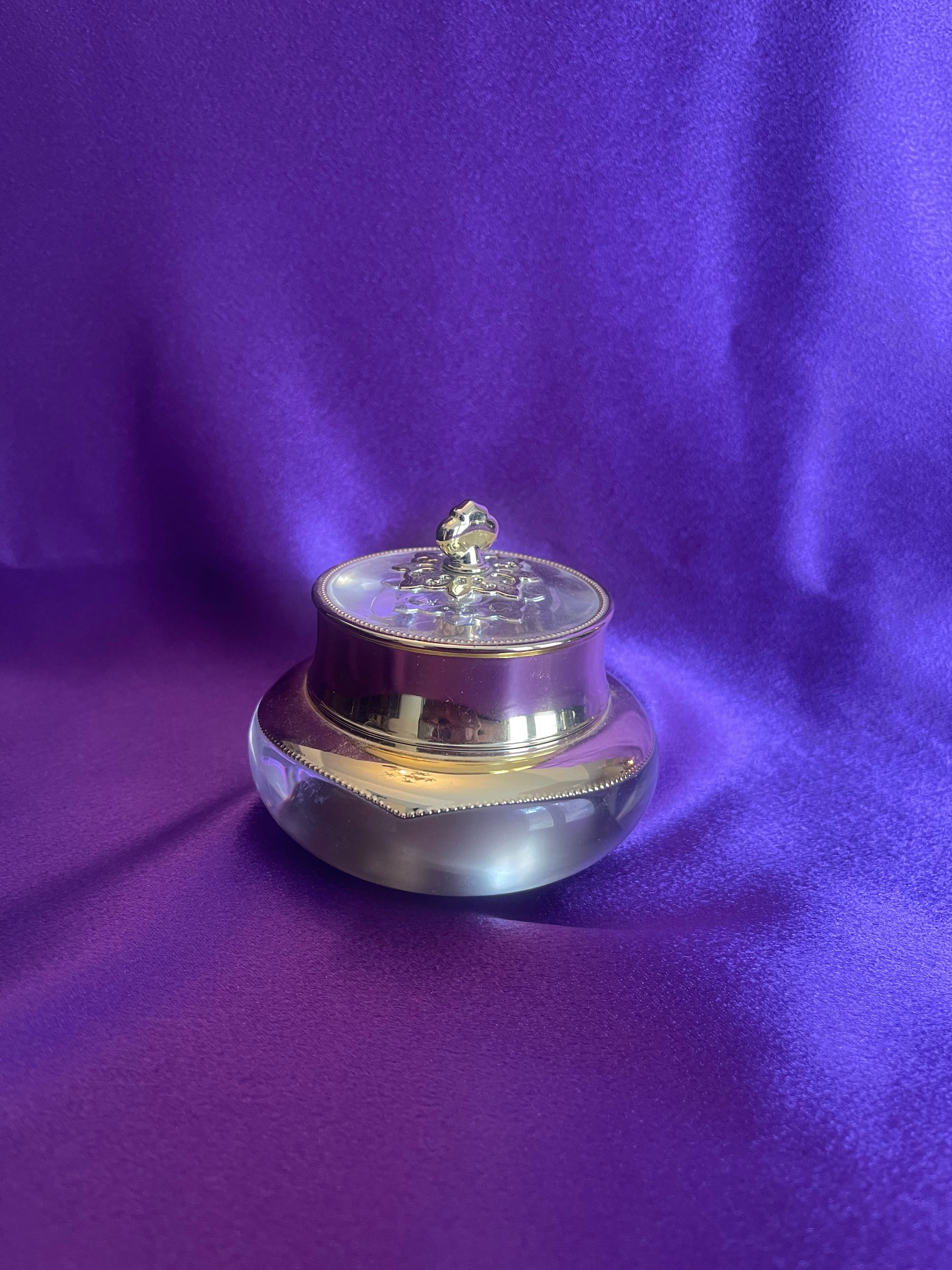 Royal Adventure Skin, Royal Secret Eye Cream Jar - Silver and gold decorative box on a purple fabric background
